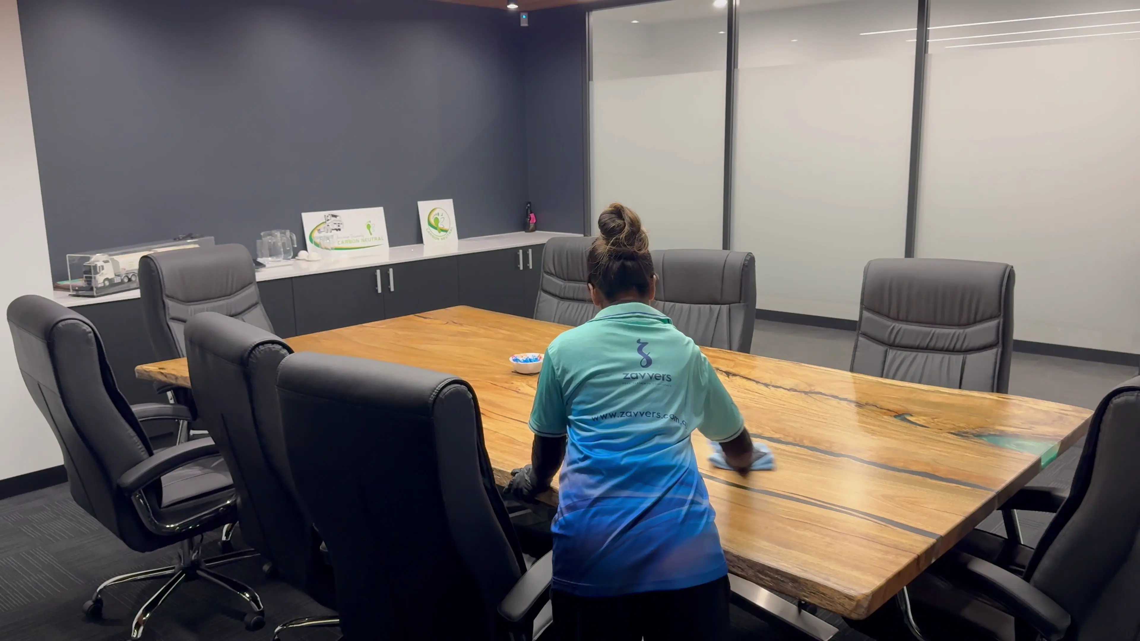 A Zavvers cleaner wiping a boardroom table surrounded by office chairs