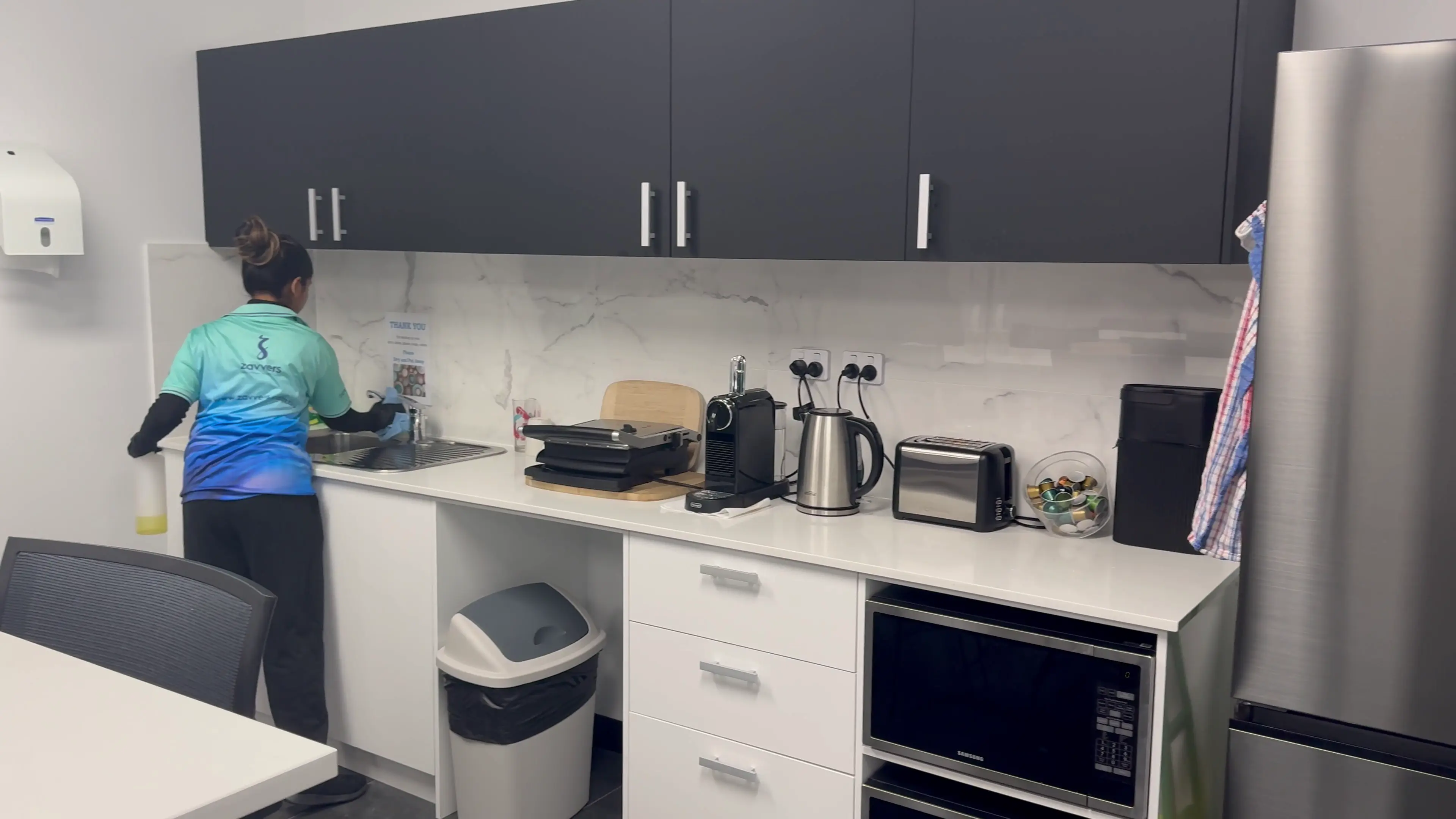 A Zavvers cleaner wiping the sink and tap in an office kitchen