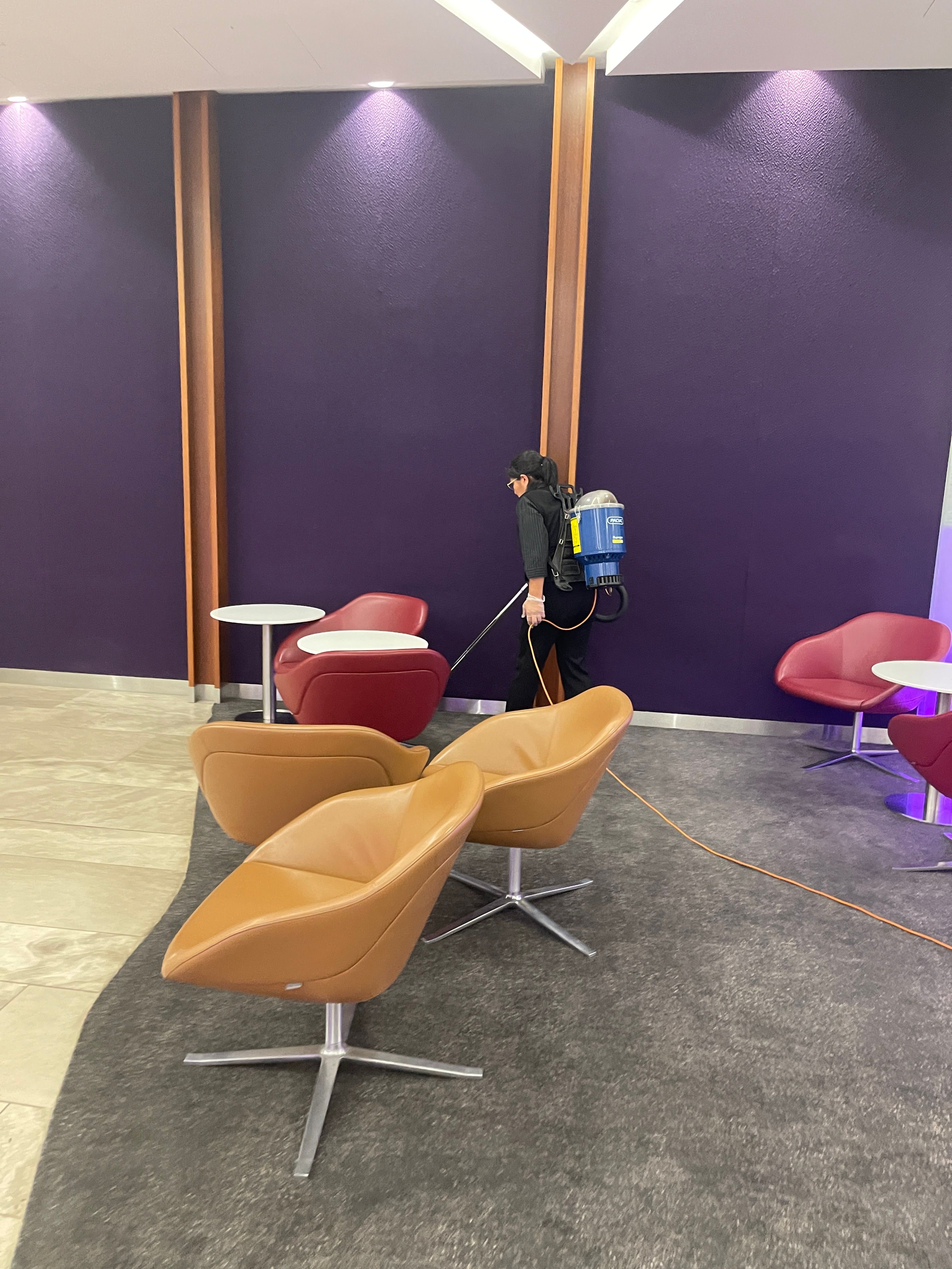 A Zavvers cleaner vacuuming a furnished workplace lounge
